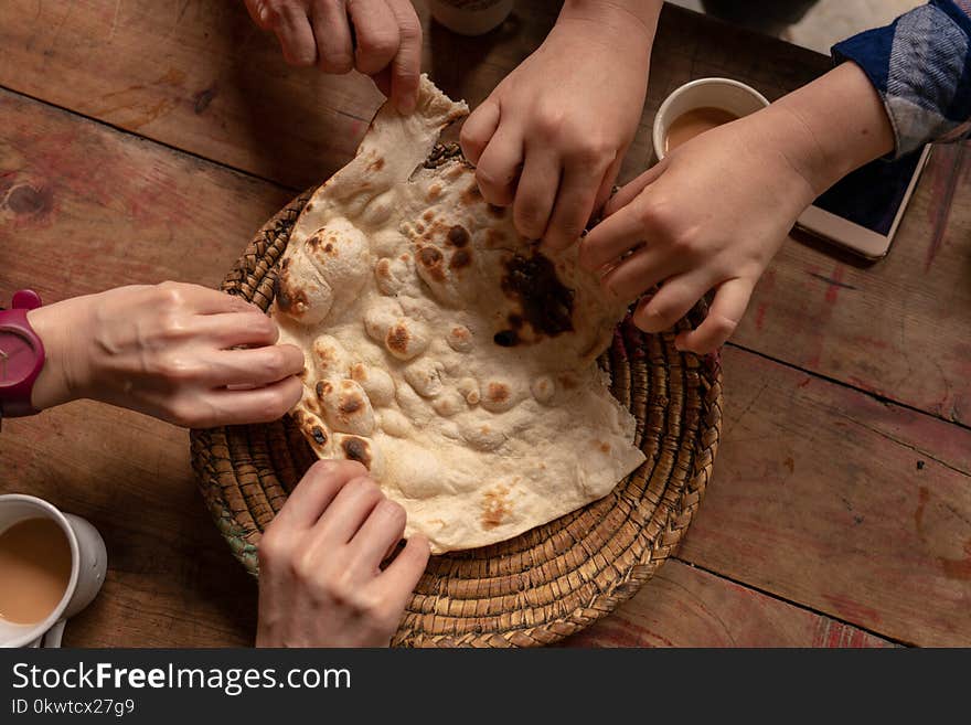 Six hands taking a piece of delicious naan Pita bread on a wooden table