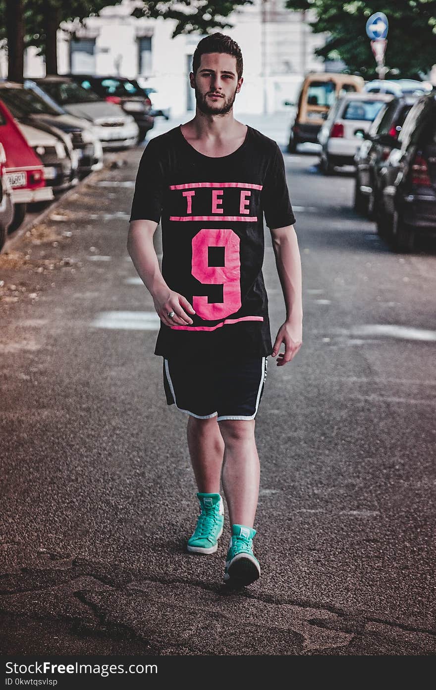 Man Wearing Black Crew-neck T-shirt, Black Shorts, and Pair of Teal High-top Sneakers Walking Between Vehicles