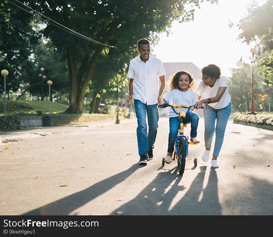 Man Standing Beside His Wife Teaching Their Child How to Ride Bicycle