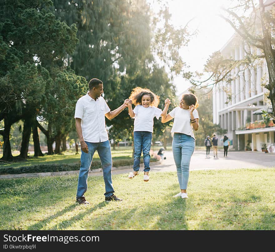 A Man and a Woman Assisting a Girl While Jumping