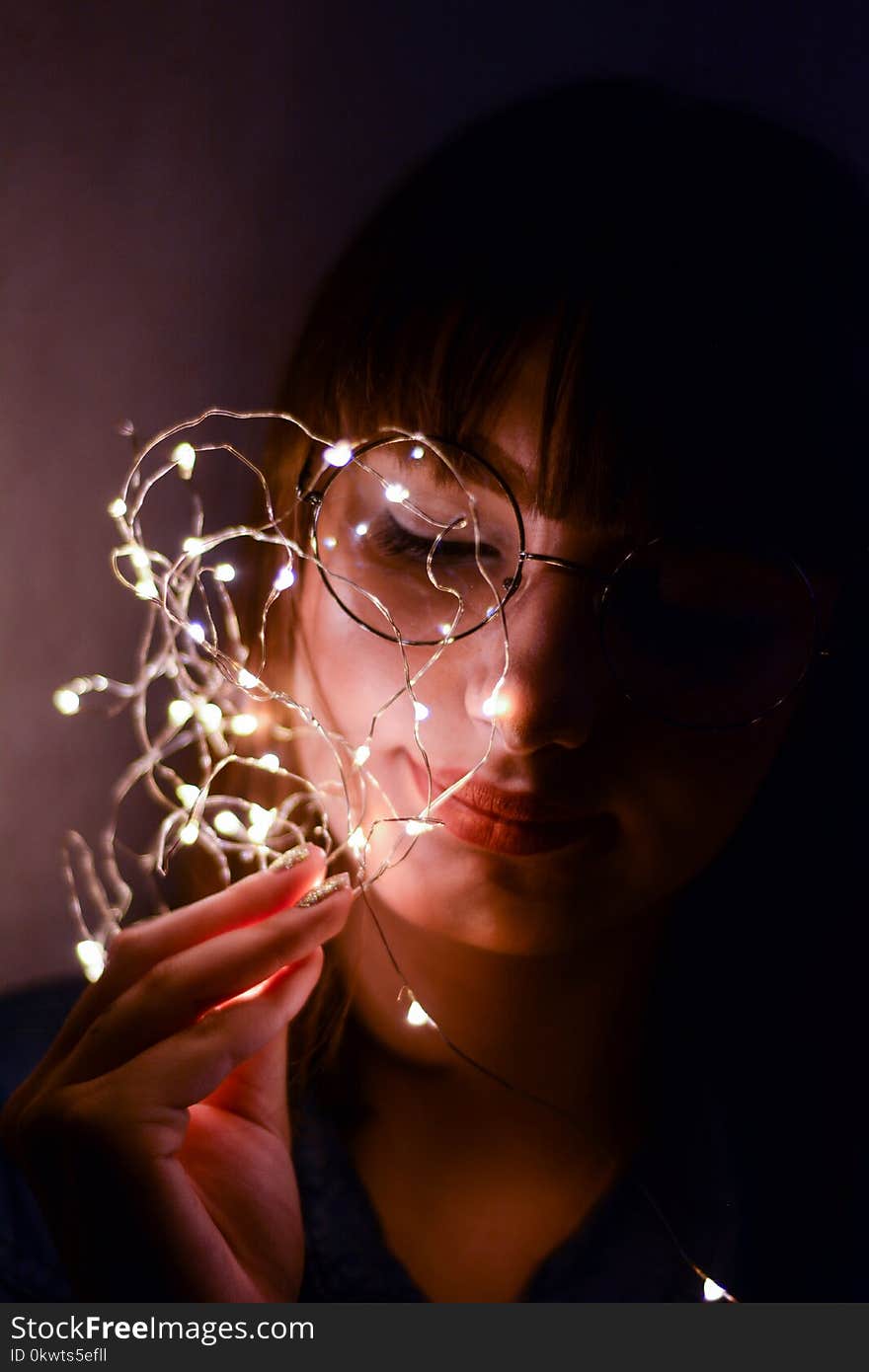 Woman in Black Shirt Leaning on Wall Holding Light Strings