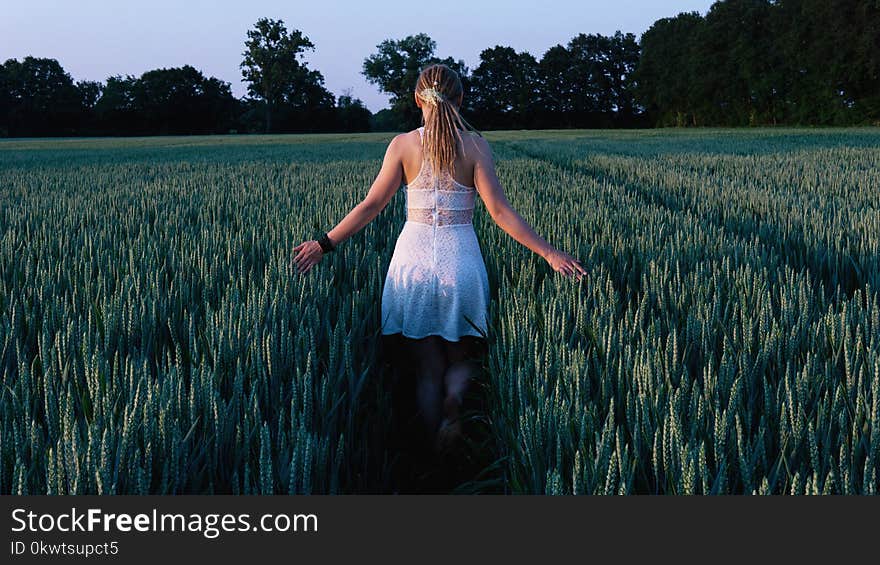 Woman in White Sleeveless Mini Dress Standing Between Grass Field