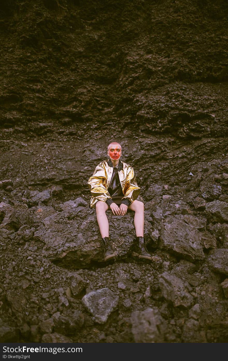 Man Wearing Gold Jacket Sitting on Stone