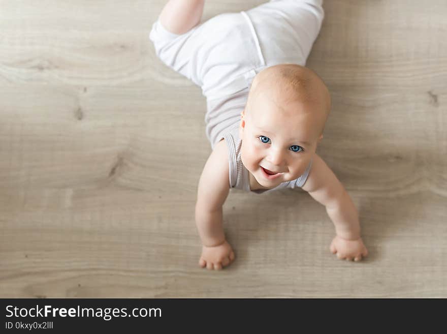 Cute little baby boy lying on hardwood and smiling. Child crawling over wooden parquet and looking up with happy face. View from above. Copyspace.