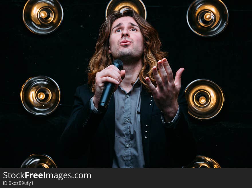 Brutal singer with microphone on the stage, with long hair, against the background of bright lanterns, scene. Brutal singer with microphone on the stage, with long hair, against the background of bright lanterns, scene