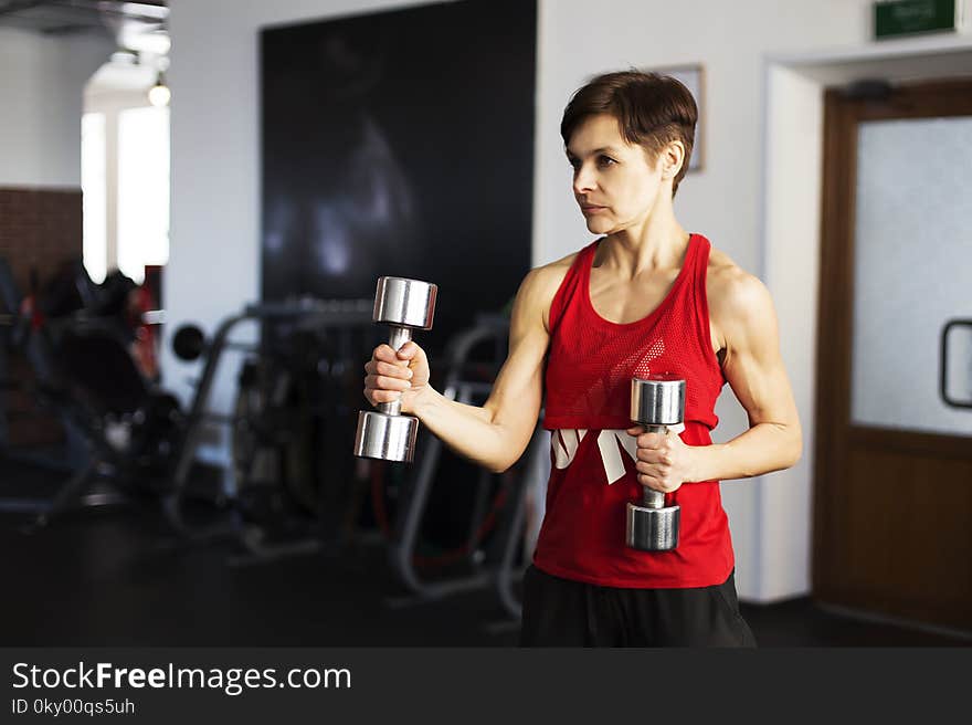 The woman in the gym doing exercises with dumbbells