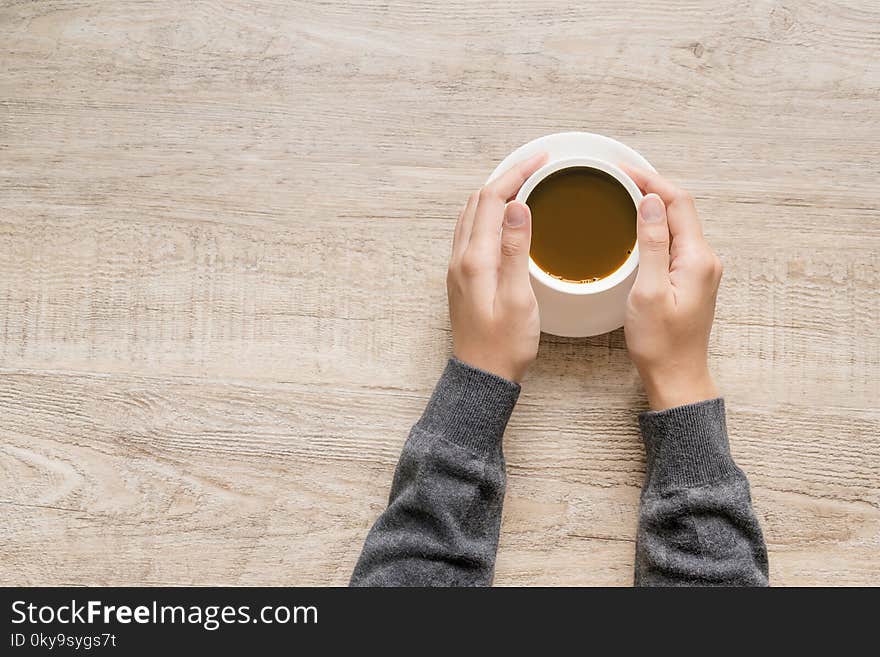 A cup of coffee in hand of women on wooden texture background.