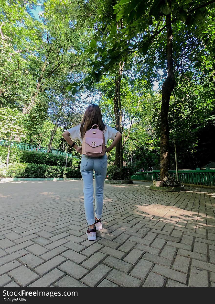 Woman Wearing White Shirt and Pink Bag Walking on Concrete Pavement