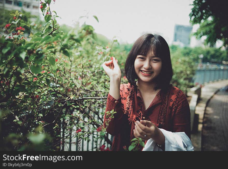 Woman Wearing Red Collared Shirt Standing Beside Plant