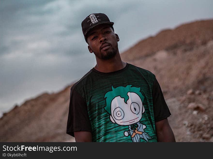 Man in Black and Green Crew-neck T-shirt Standing on Mountain Selective Focus Photography