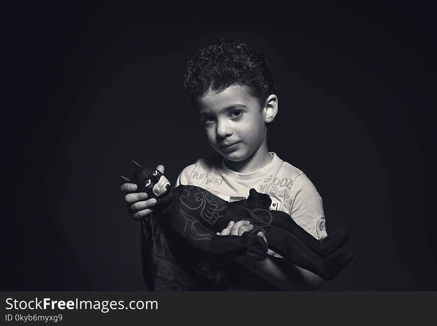 Grayscale Photo of a boy Holding Batman Plush Toy