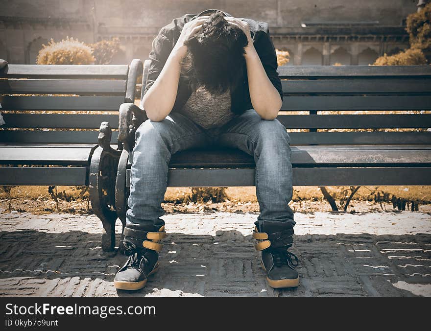 Man in Black Shirt and Gray Denim Pants Sitting on Gray Padded Bench