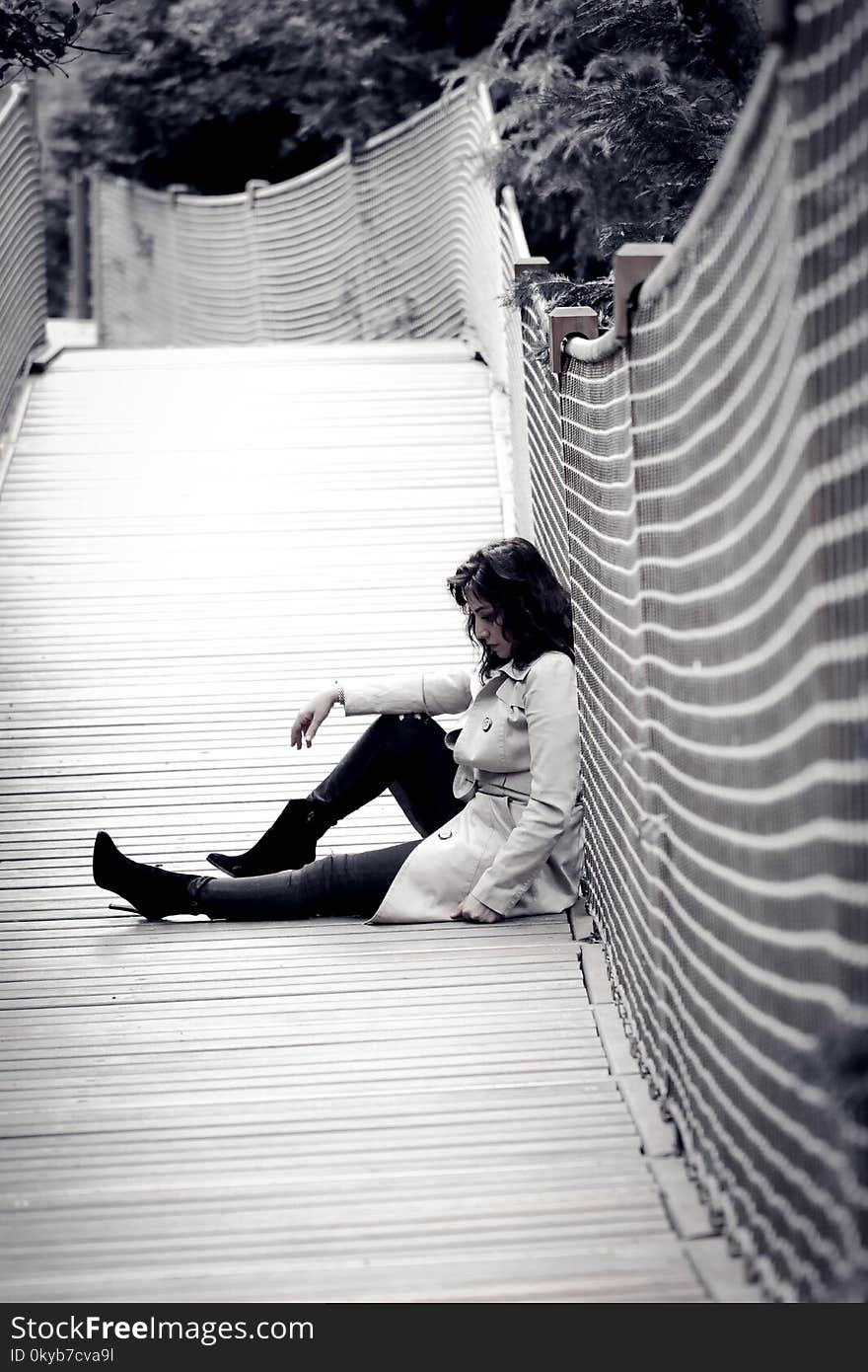 Low Light Photo of Woman Wearing Trench Coat Sitting Against Wall