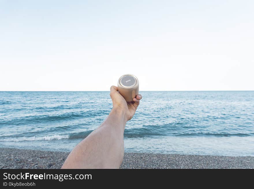 Person Holding Upward Brown Speaker in Front of Sea