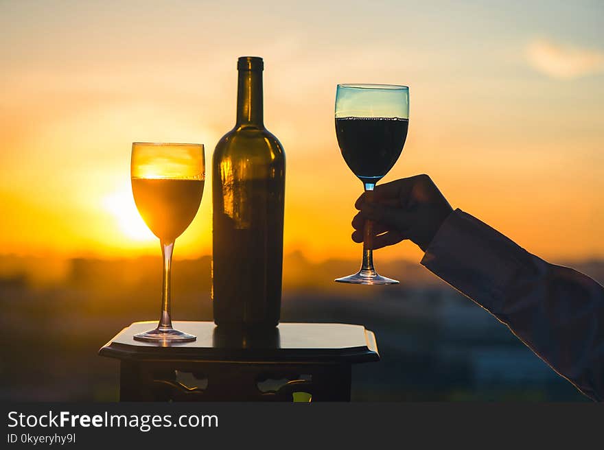 Silhouette of female hand toasting wine on sunset background. Romantic couple celebrating at a restaurant