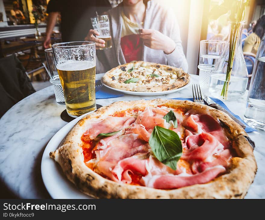 Woman drinking beer and eating delicious pizza Salsiccia e Carciofi made from Artichoke heart, Campania buffalo mozzarella, black pork sausage, pecan and San Marzano DOP tomato, Campania buffalo mozzarella sunlight flare. Woman drinking beer and eating delicious pizza Salsiccia e Carciofi made from Artichoke heart, Campania buffalo mozzarella, black pork sausage, pecan and San Marzano DOP tomato, Campania buffalo mozzarella sunlight flare