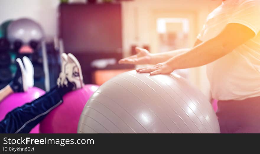 Exercising with personal trainer on large stability ball in studio fitness back physiotherapy