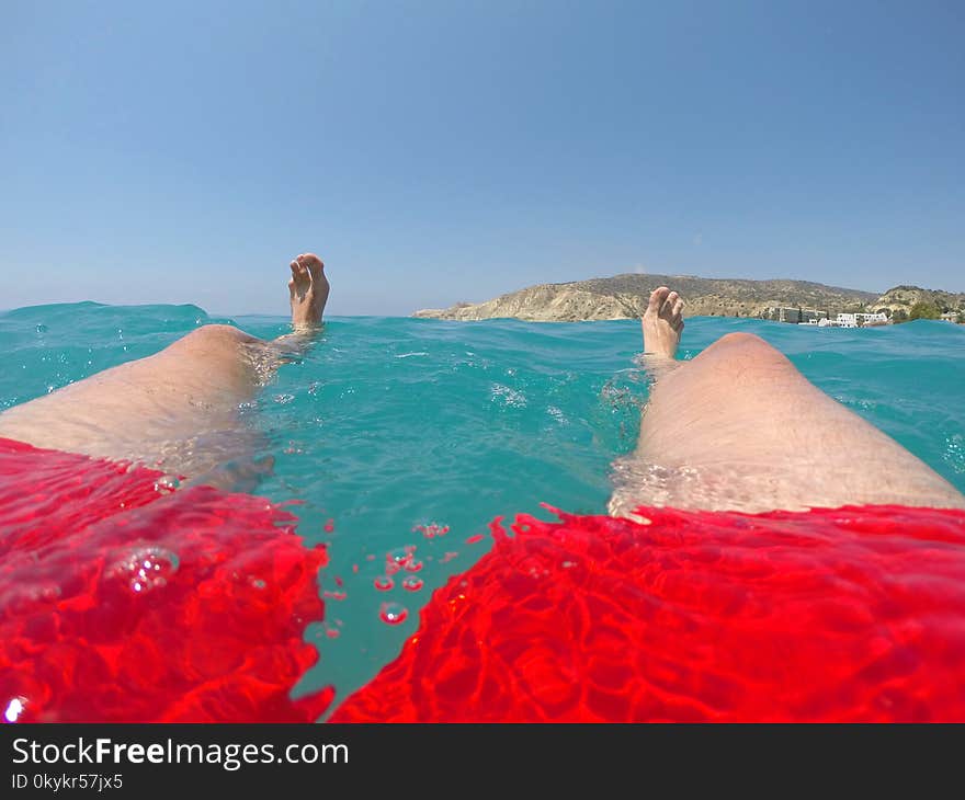 Man floating on sea water. Feet and legs of a swimmer in red swimwear floating in the sea