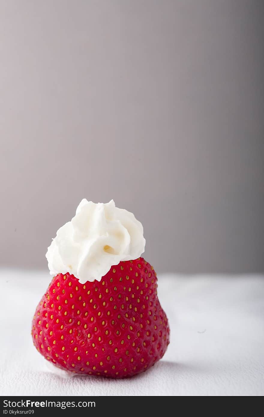 Single strawberry with whipped cream on a white grey background. Vertical image. Copy space