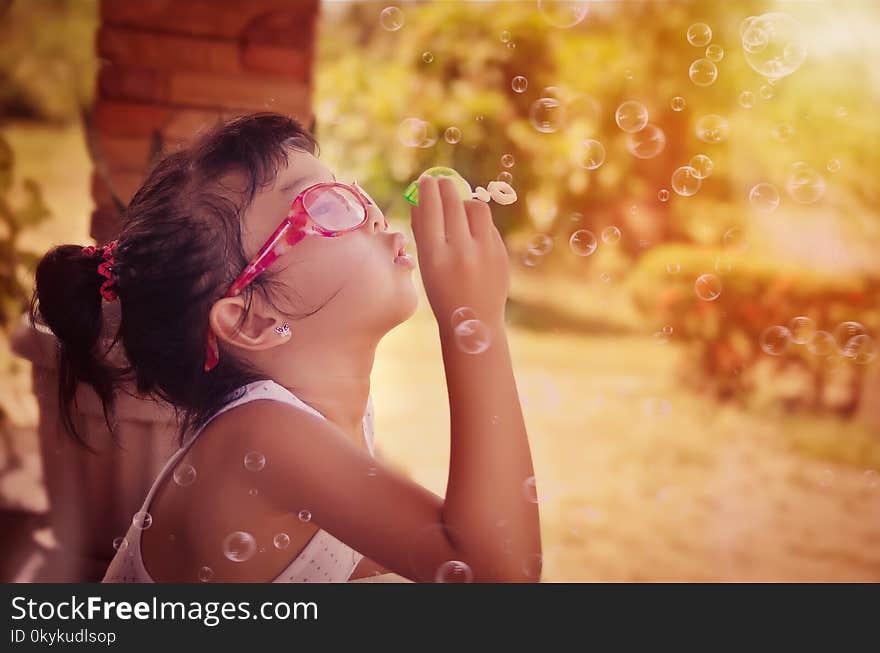 A young girl is playing with soap bubbles, wearing a pair of sunglasses to protect her eyes it. A young girl is playing with soap bubbles, wearing a pair of sunglasses to protect her eyes it.