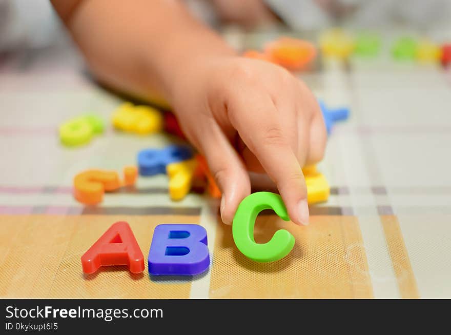 English Alphabet plastic colorful letters laid on the table with a child`s hand holding the letter C. English Alphabet plastic colorful letters laid on the table with a child`s hand holding the letter C.