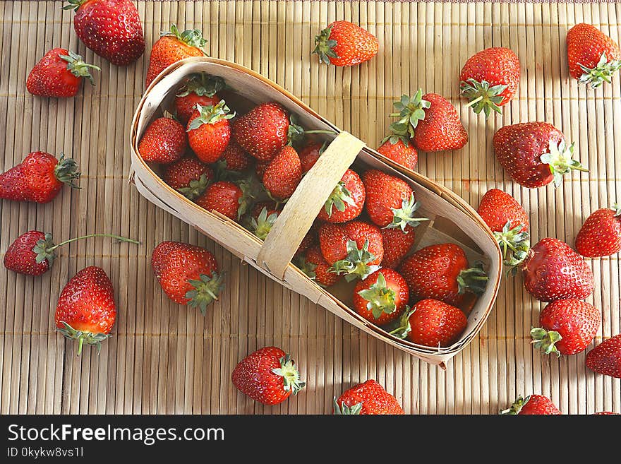 Garden strawberry from the basket is scattered on the table on a straw napkin, summer seasonn. Garden strawberry from the basket is scattered on the table on a straw napkin, summer seasonn