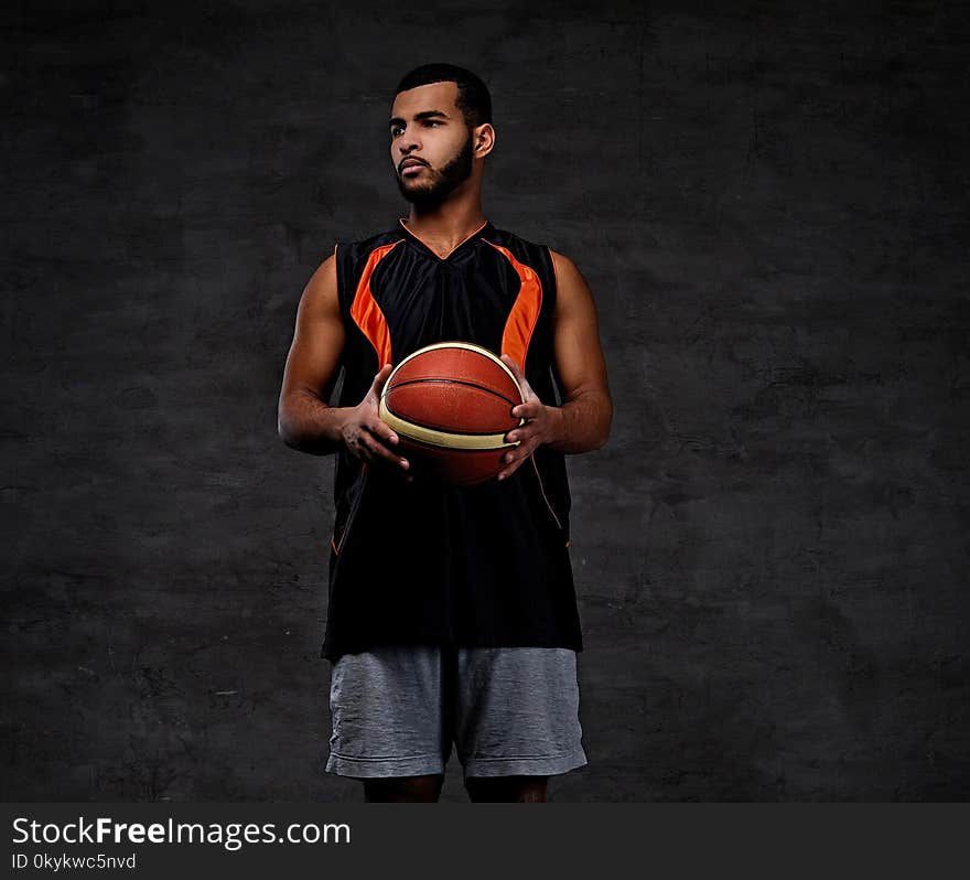 Portrait of a young African-American basketball player in sportswear over dark background.