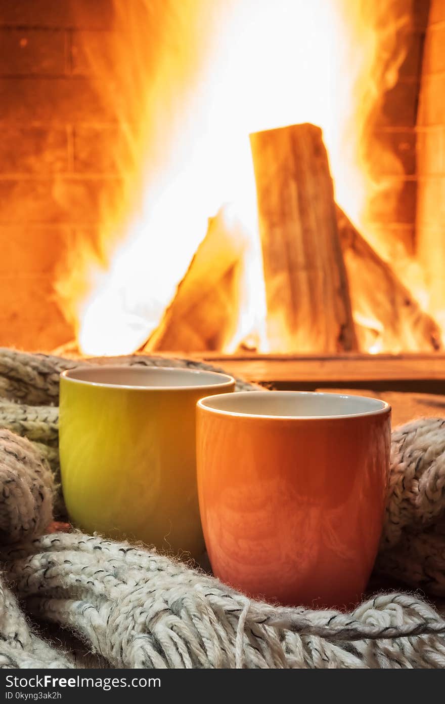 Two mugs for tea or coffee, woolen things near cozy fireplace, in country house, winter vacation, vertical. Two mugs for tea or coffee, woolen things near cozy fireplace, in country house, winter vacation, vertical.