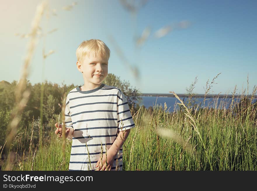 Little blond boy smiling and looking at camera on nature. Summer activity. Field with high grass. Little blond boy smiling and looking at camera on nature. Summer activity. Field with high grass.