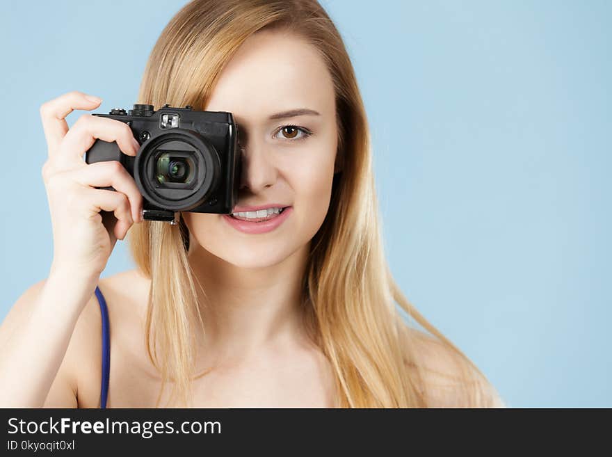 Photographer girl shooting images. Lovely blonde smiling woman with camera on blue background. Photographer girl shooting images. Lovely blonde smiling woman with camera on blue background