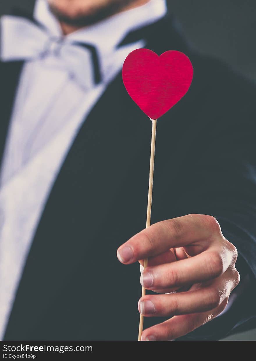 Valentines day. Love concept. Holidays and celebration. Elegant young guy wearing suit white shirt bow tie holding heart stick in hand. Valentines day. Love concept. Holidays and celebration. Elegant young guy wearing suit white shirt bow tie holding heart stick in hand