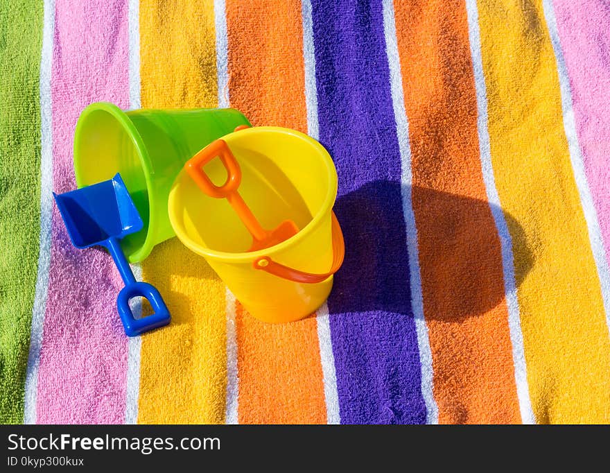 2 plastic sand pails and shovels on top of a colorful striped beach towel on a sunny summer day. 2 plastic sand pails and shovels on top of a colorful striped beach towel on a sunny summer day