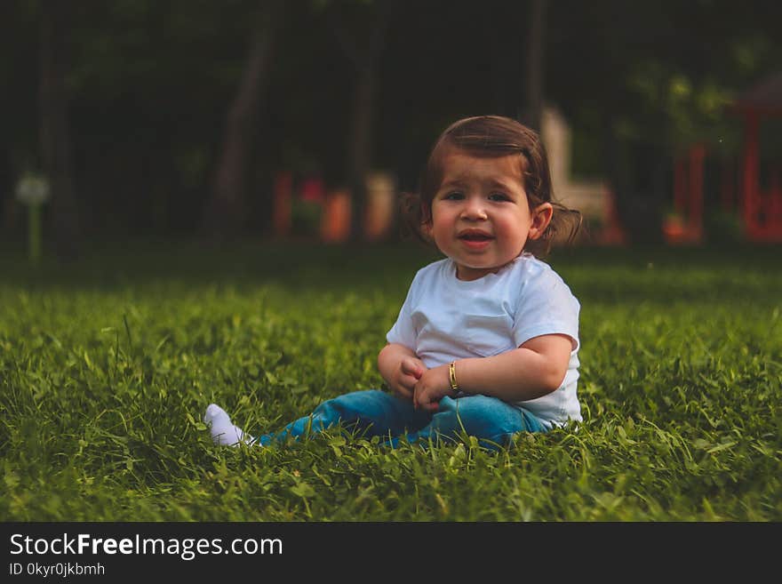 Girl Wearing White T-shirt And Blue Pants Sitting On Green Grass