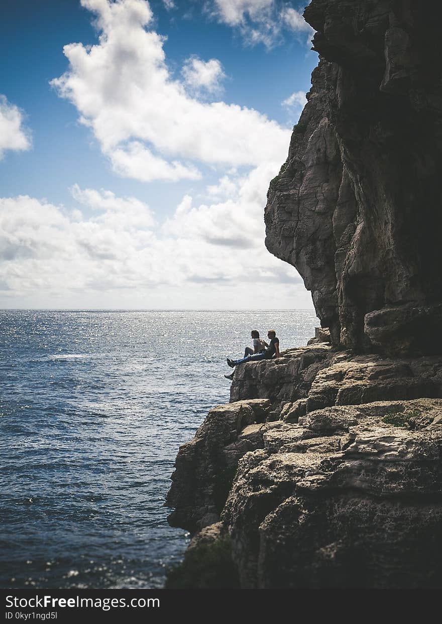 Two People Sitting By The Cliff