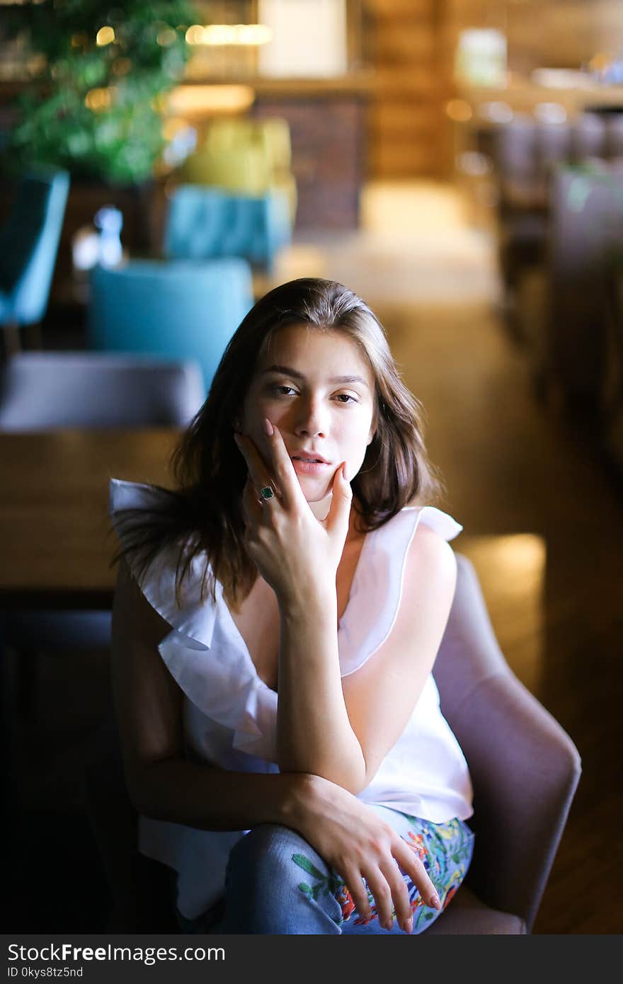 Stylish photo model sitting at cafe and wearing white blouse with ethnic jeans. Concept of fashion and beauty.