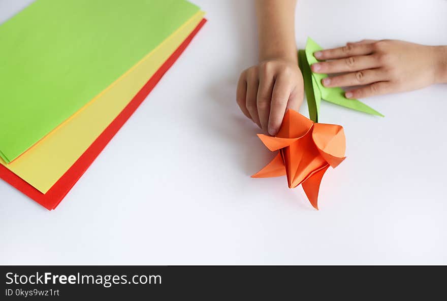 Children`s hands do origami from colored paper on white background. lesson of origami