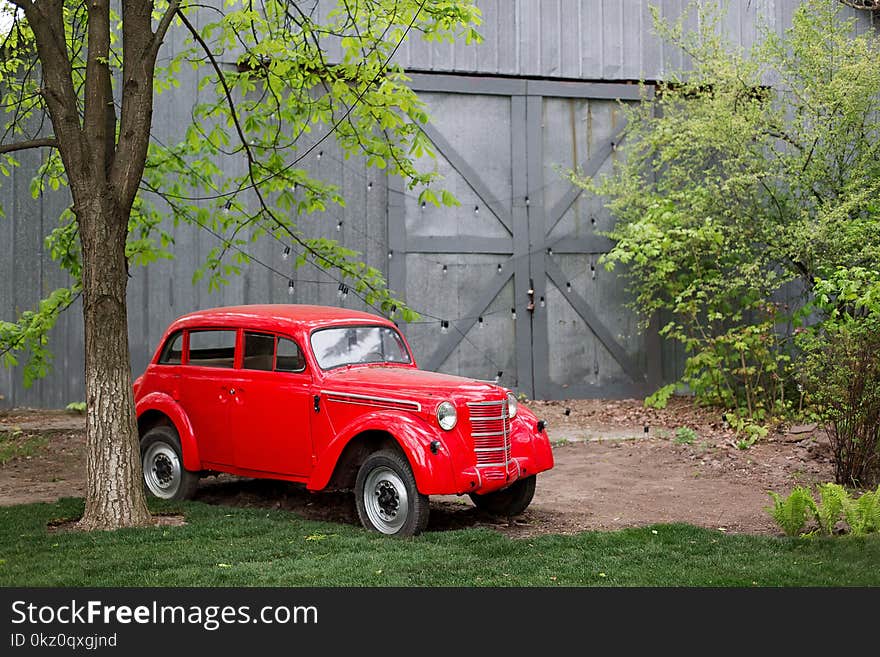 Red retro small vintage car standing in the garden in the summer. Location