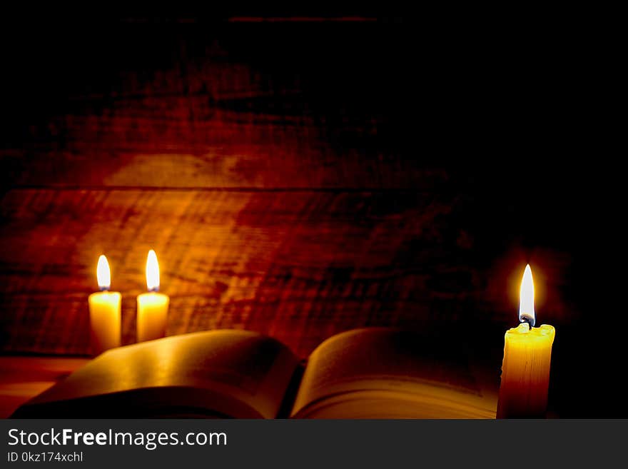 Old book on a wooden table by candlelight