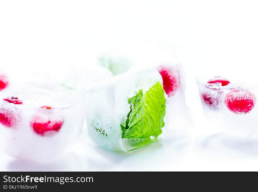 Ice cubes with fresh red berries and mint leaves on white table background. Ice cubes with fresh red berries and mint leaves on white table background