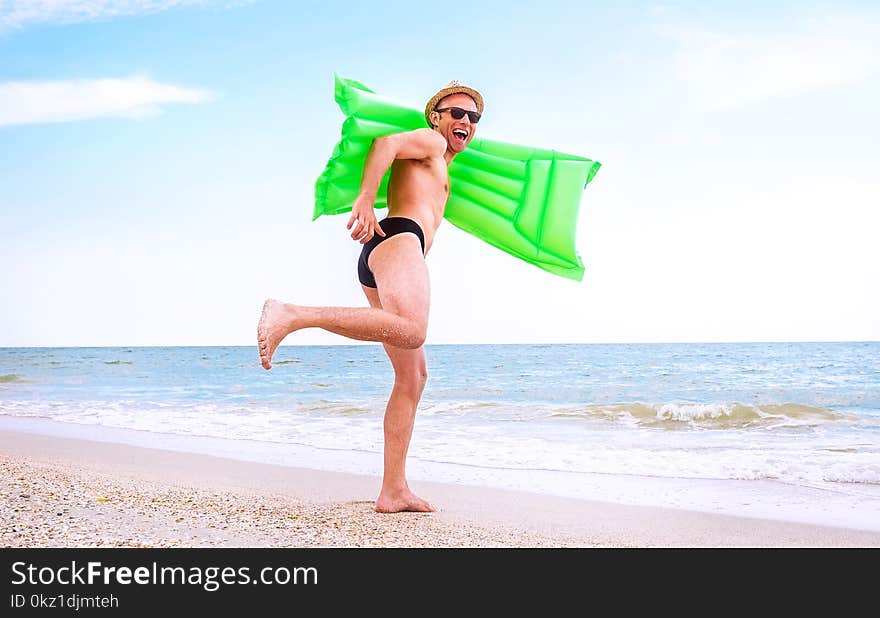 Crazy happy man with swimming mattress runs in the sea