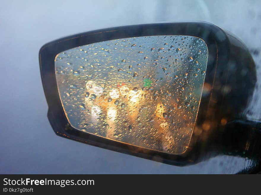 Rearview mirror with drops of water from the rain and a car with headlights. Selective focus, shallow DOF