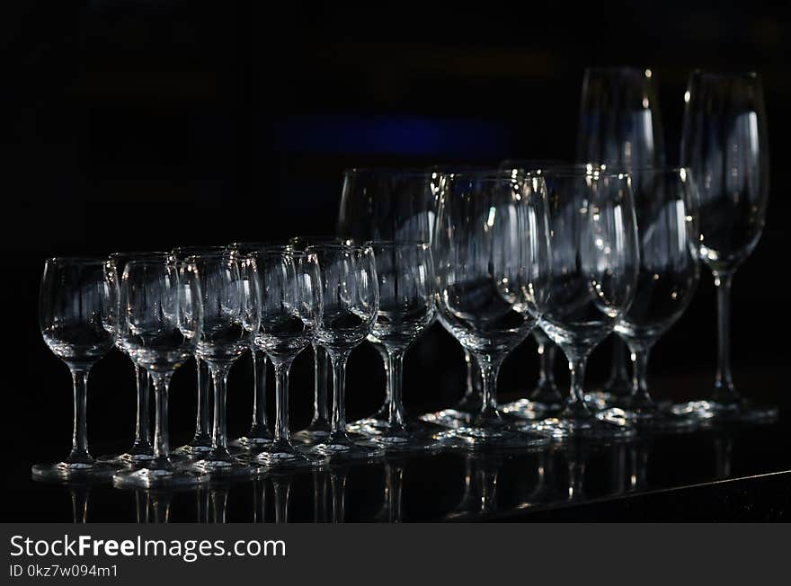 Rows of the empty wineglasses and empty glasses for vodka, going to unsharpness, stands on a black surface bar counter. Rows of the empty wineglasses and empty glasses for vodka, going to unsharpness, stands on a black surface bar counter.