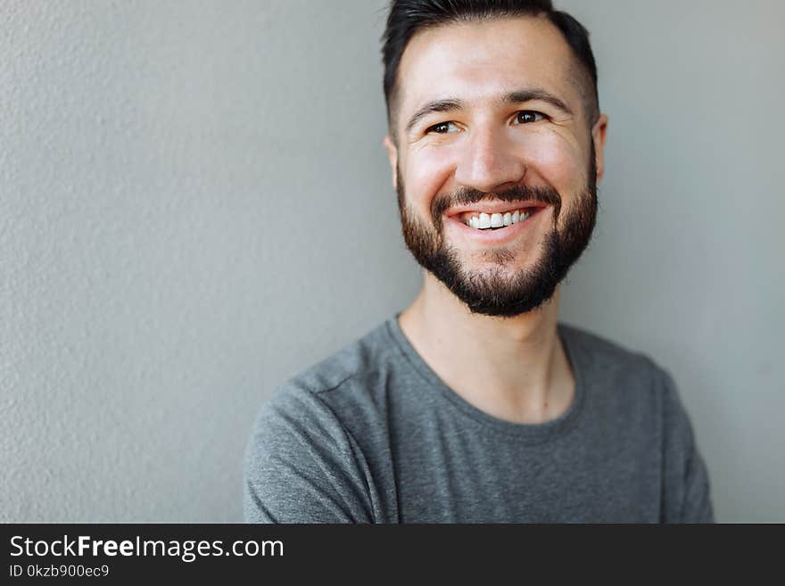 Portrait of a beautiful stylish guy dressed in a grey blank t-shirt standing on a brick grey wall background. Empty space for log