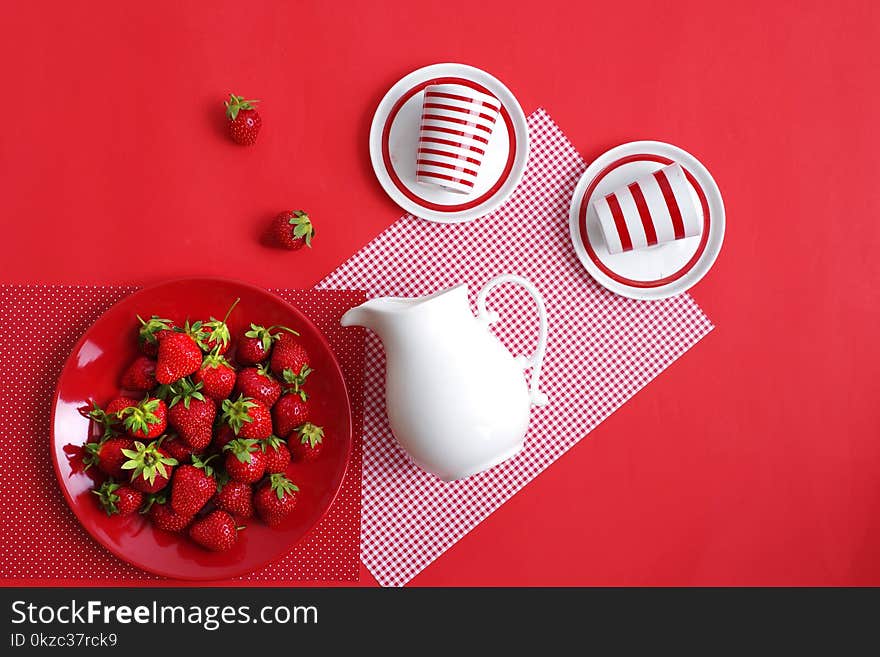 Bright red ripe summer strawberries and a white jug with cream on a red background. Top view.