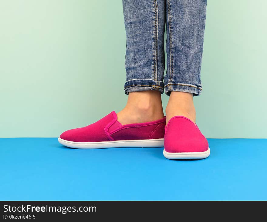 Hipster girl`s legs in jeans on the blue floor by the blue wall. Modern style. The concept of modern sports style.