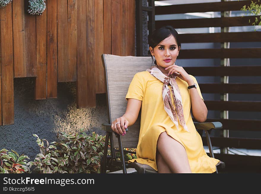 Woman Wearing Yellow Short-sleeved dress Sitting on Black Metal Armchair