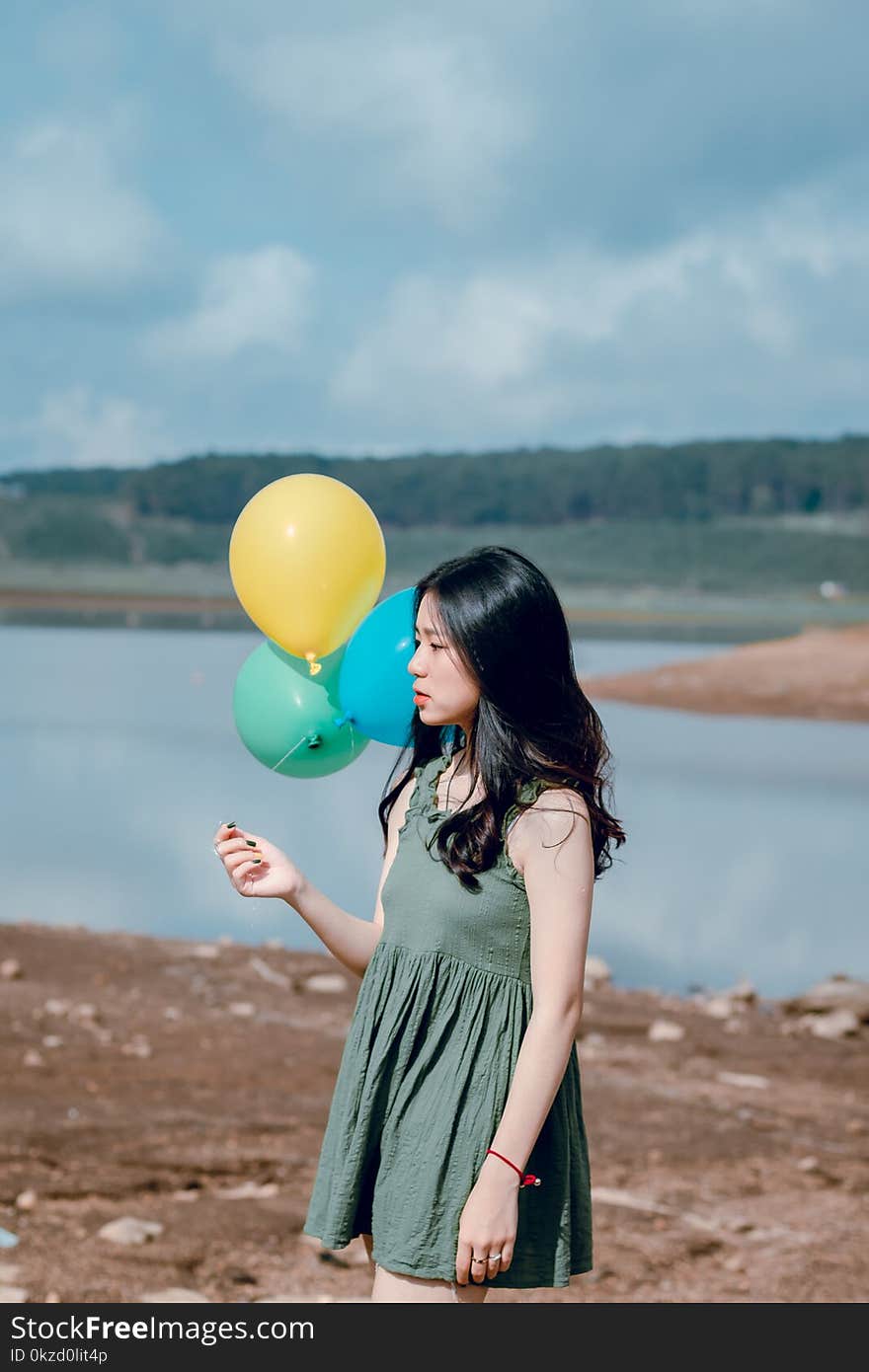 Woman in Green Sleeveless Dress Holding Yellow, Green, and Blue Balloons