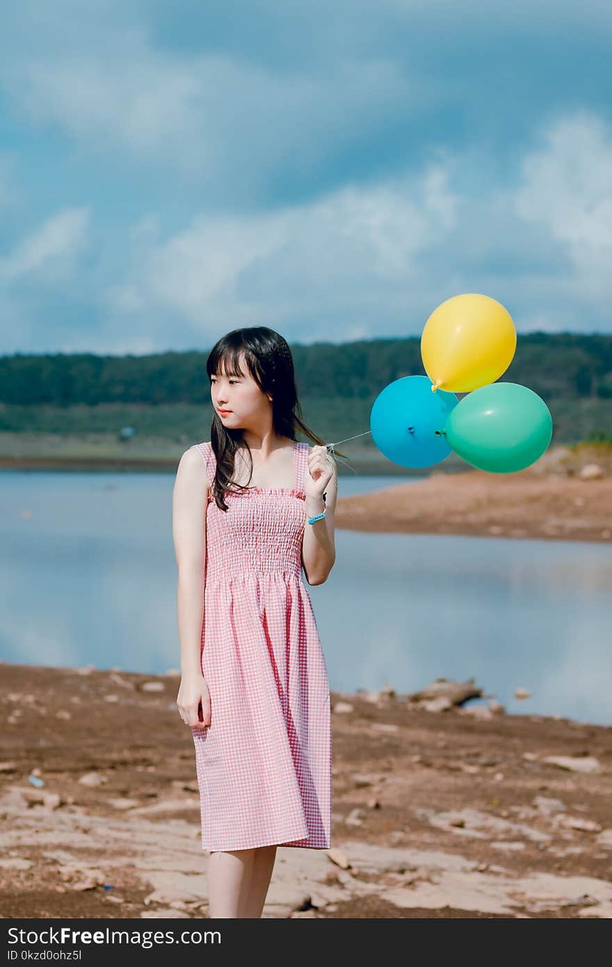 Woman Wearing Pink Dress Holding Three Balloons Near Body of Water