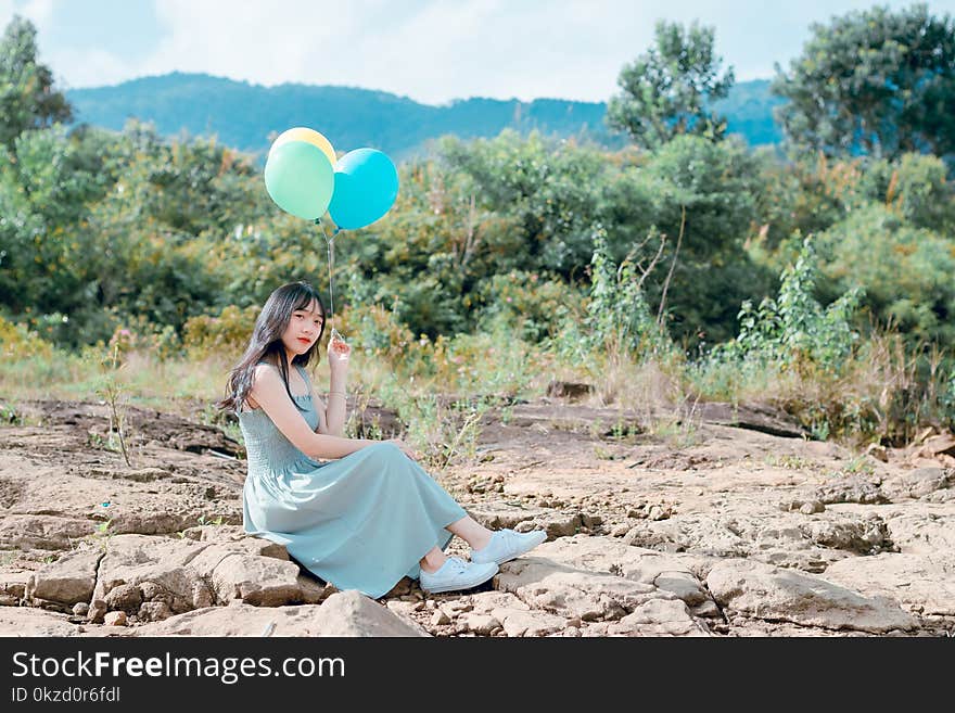 Woman Sitting On Rocks Holding Balloons