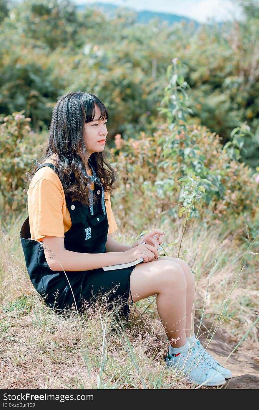 Photo of Woman Sitting on Ground Surrounded by Grass, Trees, and Plants